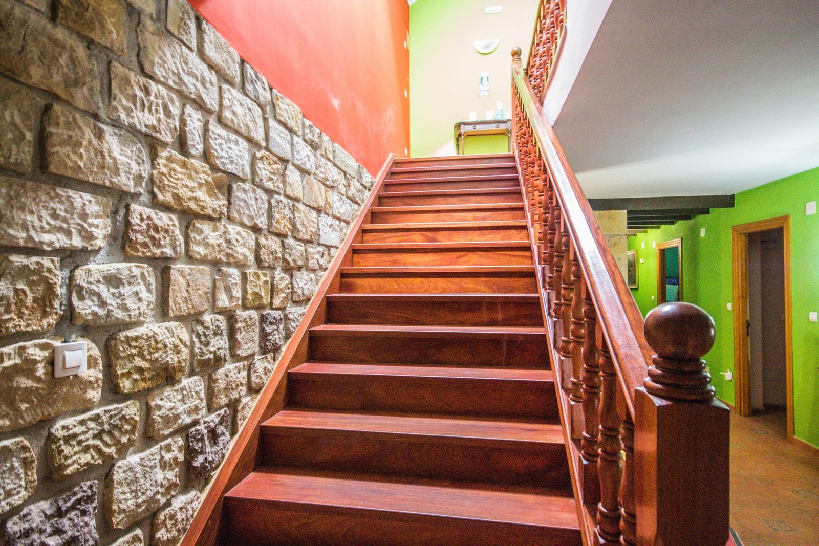 Escalera de madera noble con barandilla torneada y pared de piedra en el interior de Finca Gándara